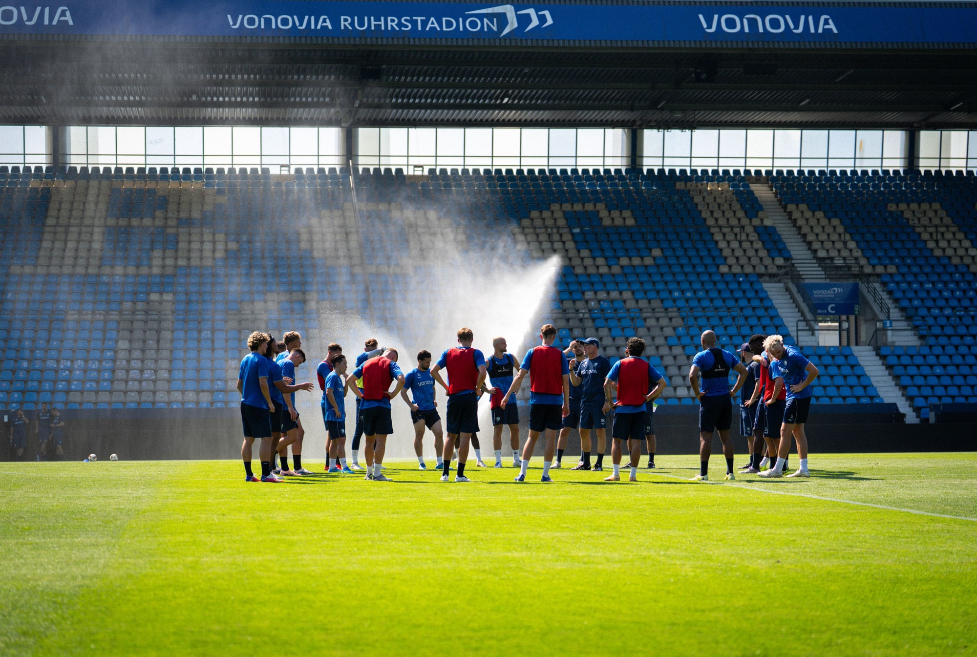 Trainingsgruppe im Vonovia Ruhrstadion bei hohen Temperaturen und einer Abkühlung im Hintergrund