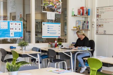 Leerkracht in het primair onderwijs zittend achter bureau in klaslokaal