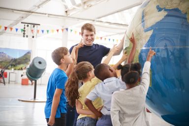 Meester met kinderen wijzend naar wereldbol