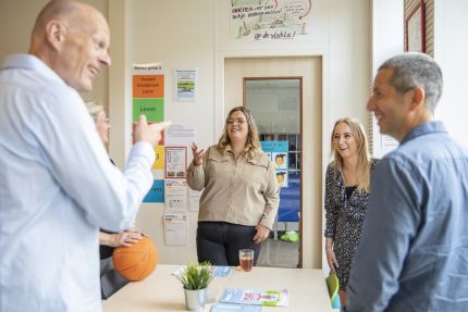 Een groep leerkrachten staat lachend om een tafel in de klas
