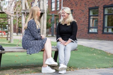 twee vrouwen op een bankje op een schoolplein die praten over inzetbaar zijn in het onderwijs