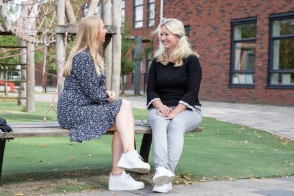 twee vrouwen op een bankje op een schoolplein die praten over inzetbaar zijn in het onderwijs