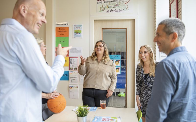 Een groep leerkrachten staat lachend om een tafel in de klas