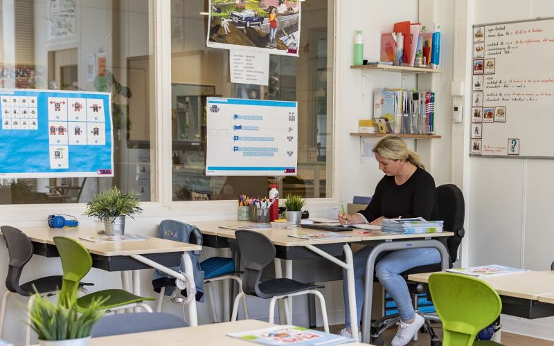 Leerkracht in het primair onderwijs zittend achter bureau in klaslokaal