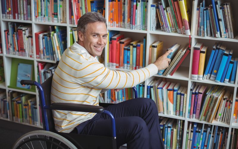 Man in rolstoel pakt een boek uit de schoolbibliotheek