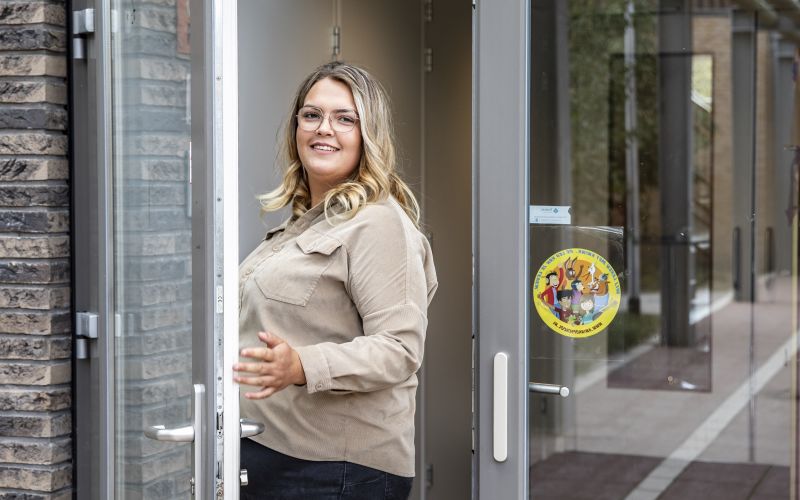 Portret van jonge leerkracht die in deuropening ingang school staat