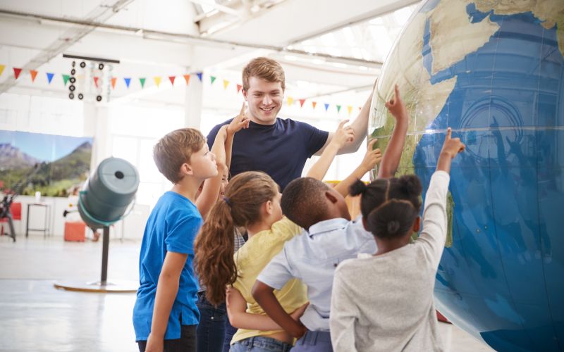 Meester met kinderen wijzend naar wereldbol