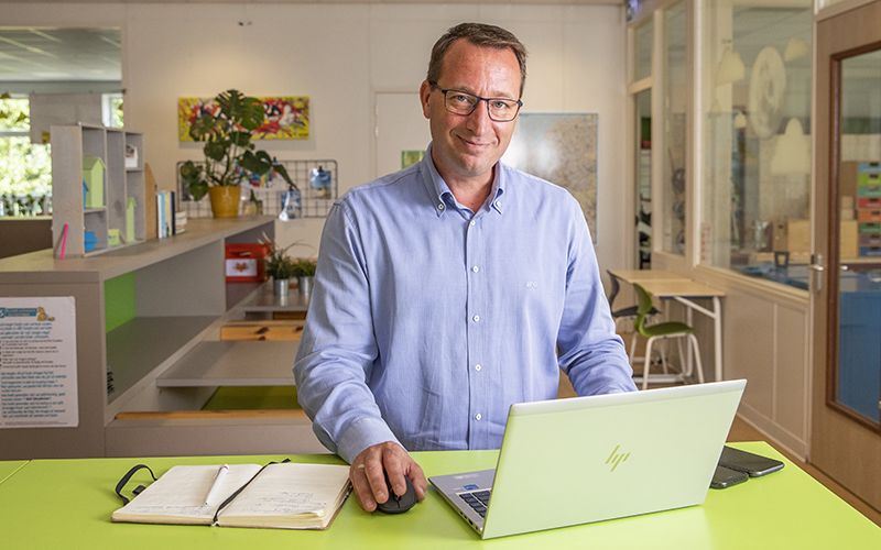 Bestuurder van een schoolorganisatie kijkt vanachter laptop glimlachend in camera