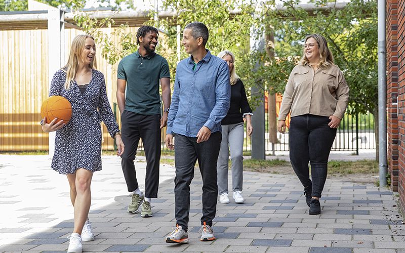 Groep leerkrachten lopen werkgelukkig buiten op het schoolplein tevreden met de schoolorganisatie