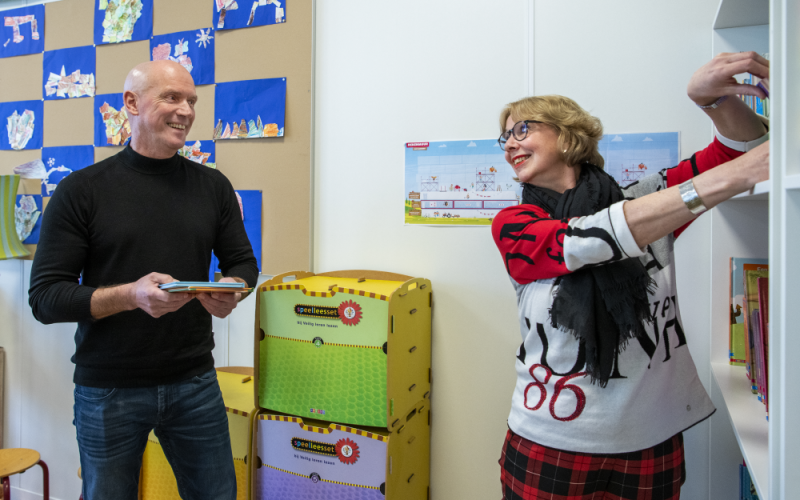 Iemand geeft boekjes aan een lerares die de boekjes in de kast plaatst