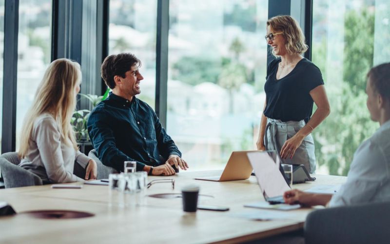 Leekrachten rond een tafel in de lerarenkamer staan te kletsen en te lachen met laptops op tafel