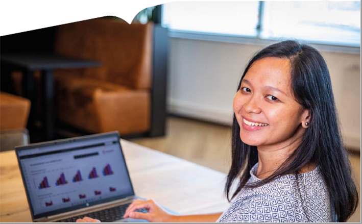 jonge vrouw achter laptop kijkt lachend in camera