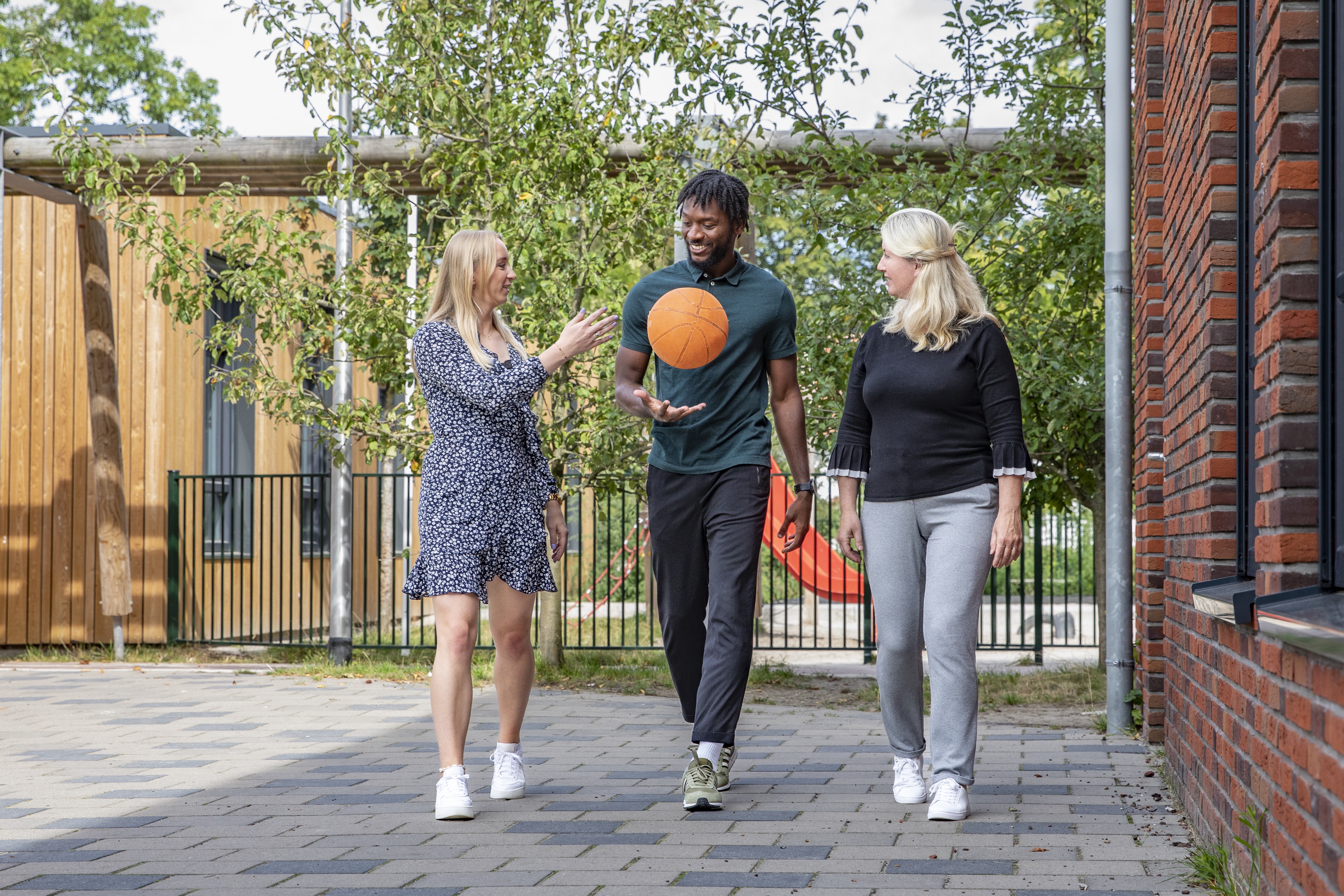 drie leraren lopen op schoolplein met basketbal