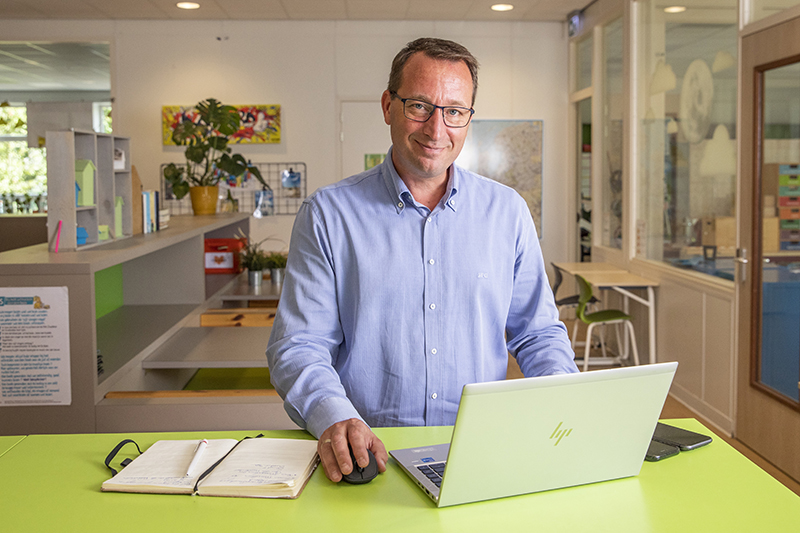 bestuurder van een schoolorganisatie kijkt vanachter laptop glimlachend in camera