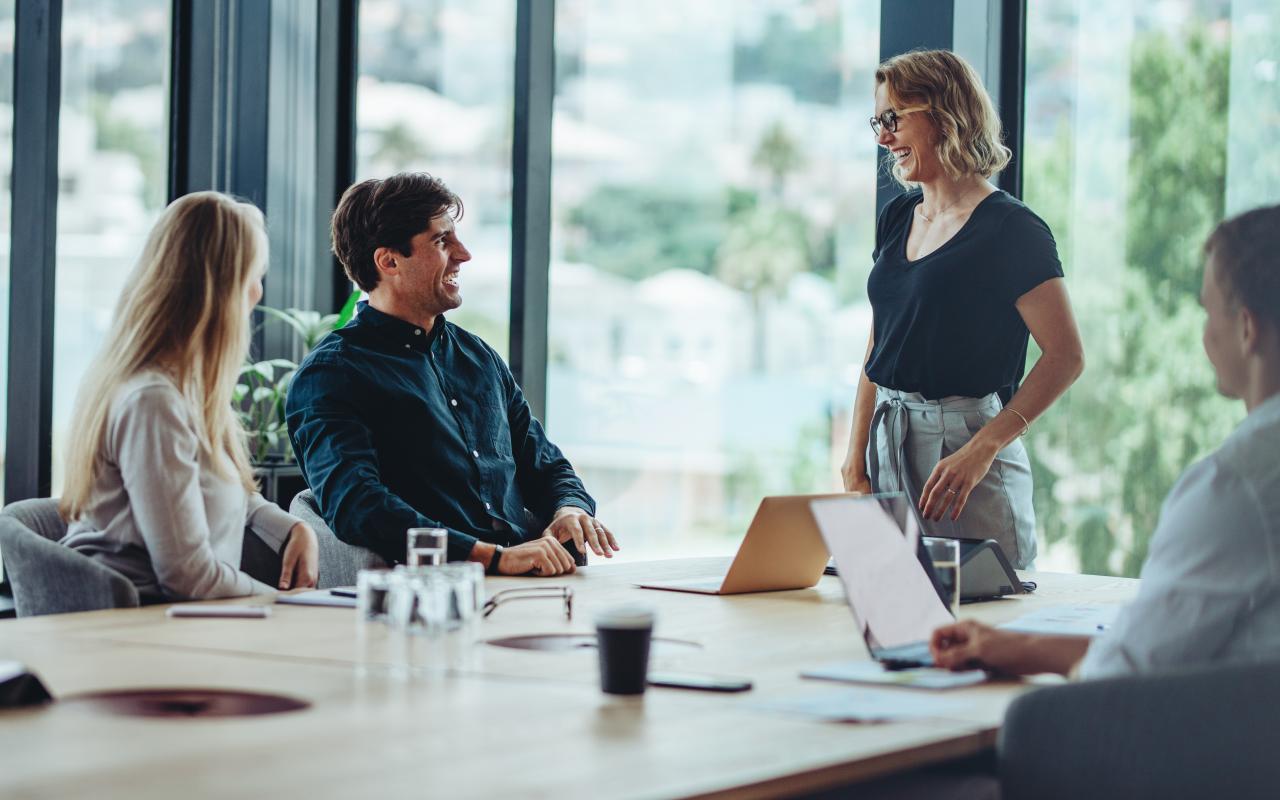 leekrachten rond een tafel in de lerarenkamer staan te kletsen en te lachen met laptops op tafel