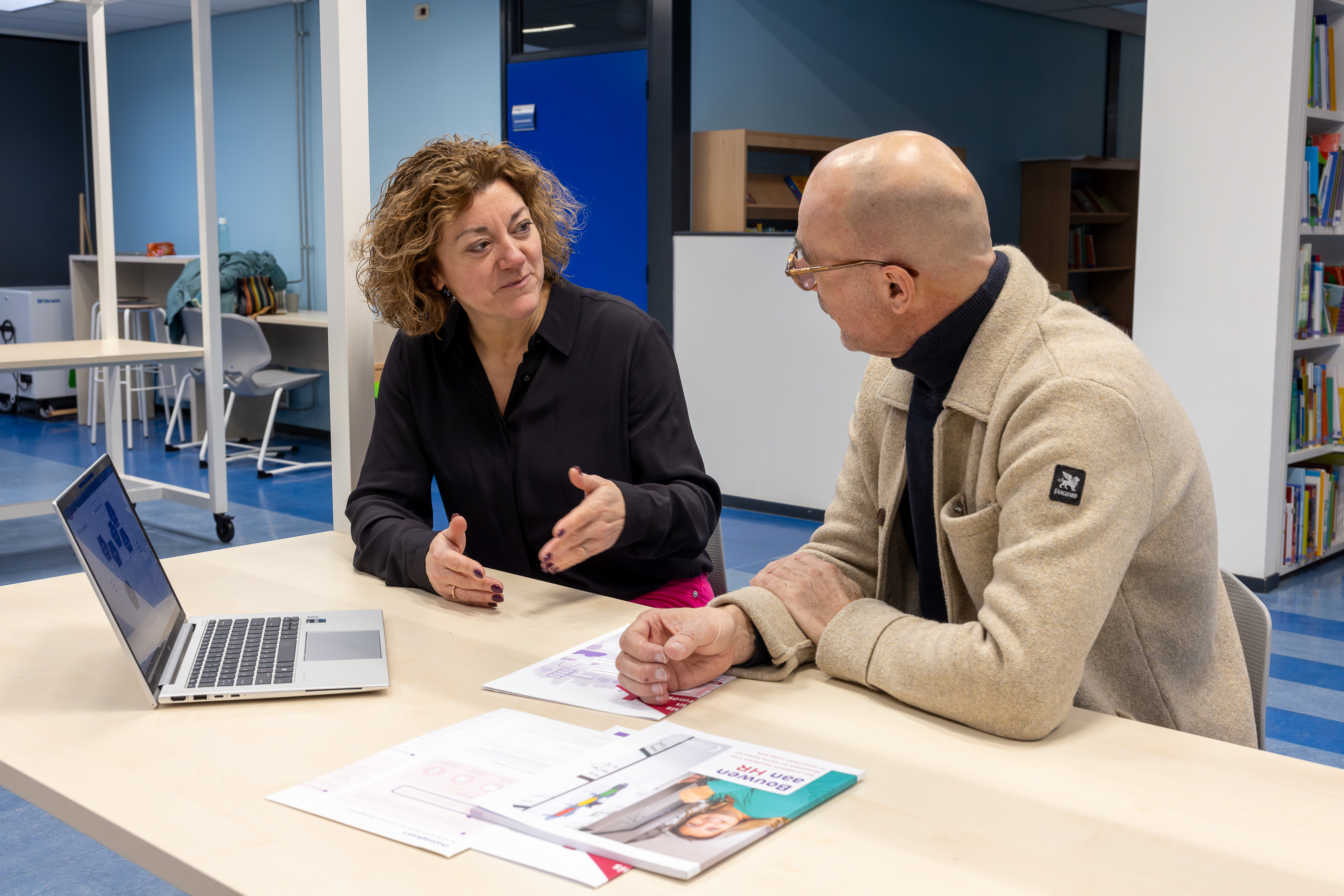 een man en een vrouw die praten en bij een laptop zitten