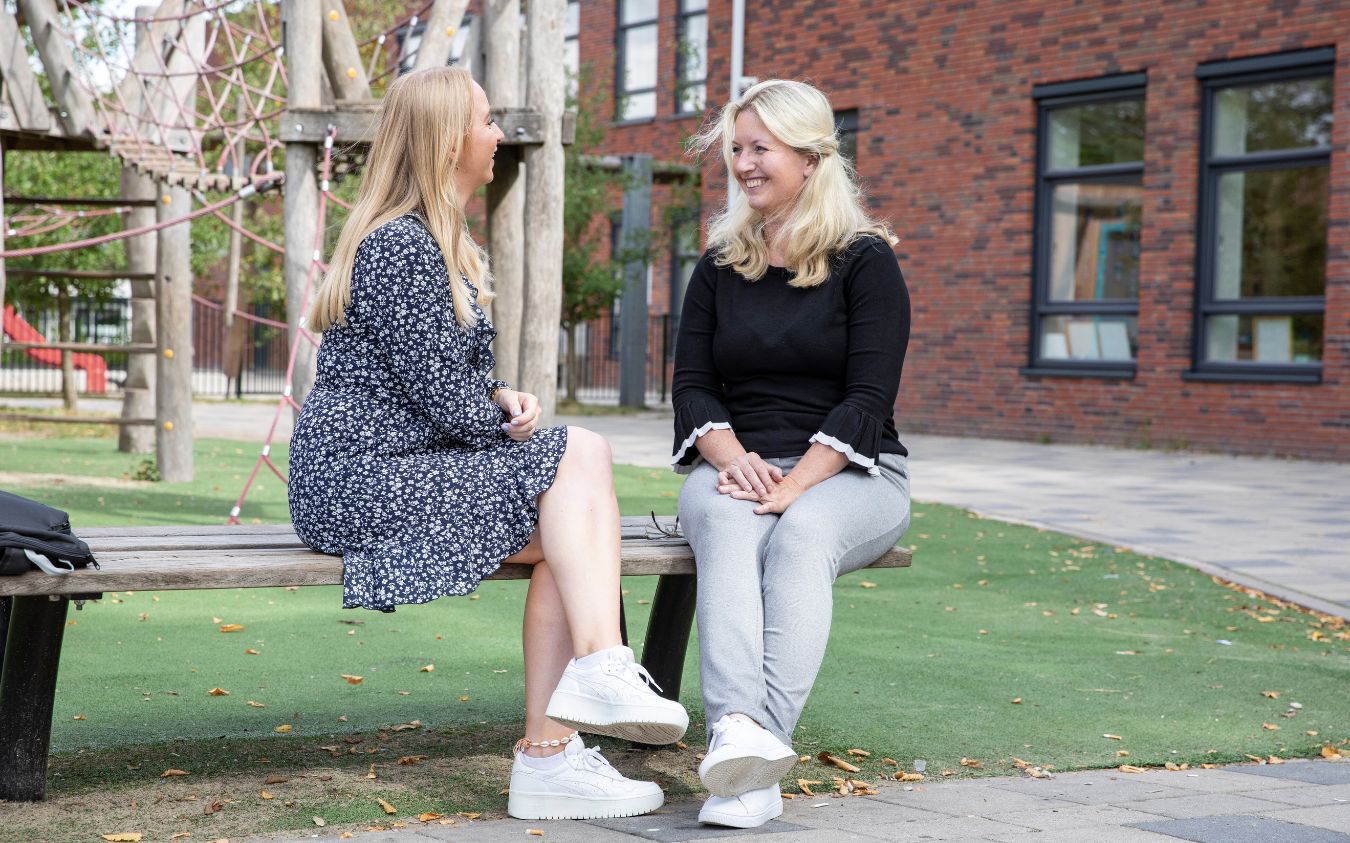 twee vrouwen op een bankje op een schoolplein die praten over inzetbaar zijn in het onderwijs