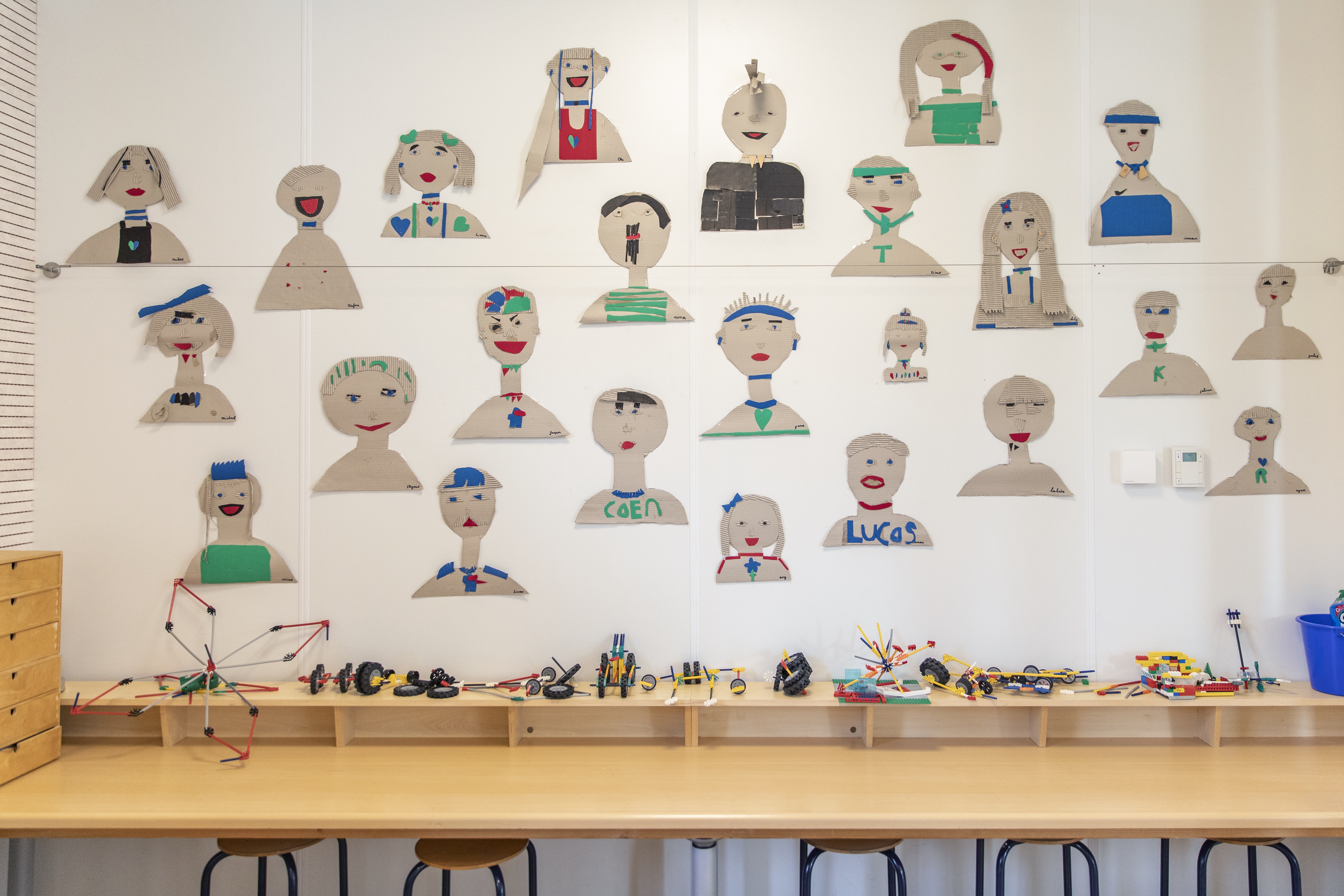 afbeelding van een knutselwerkje aan de muur met verschillende personen van karton en kleur