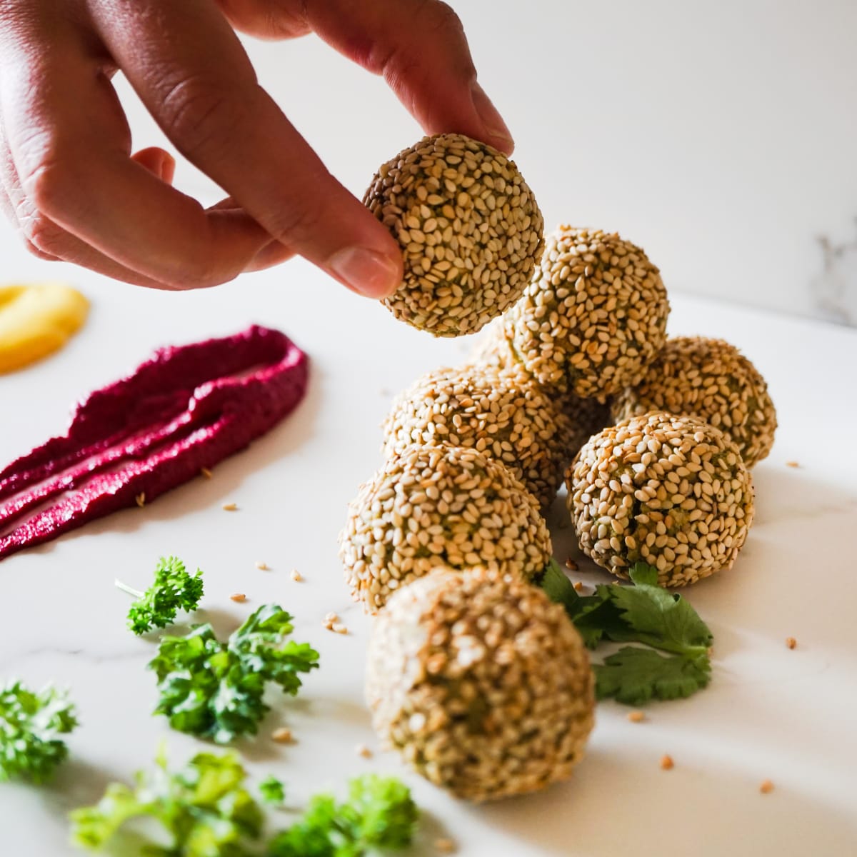 holding a falafel ball with colorful tahini on the background