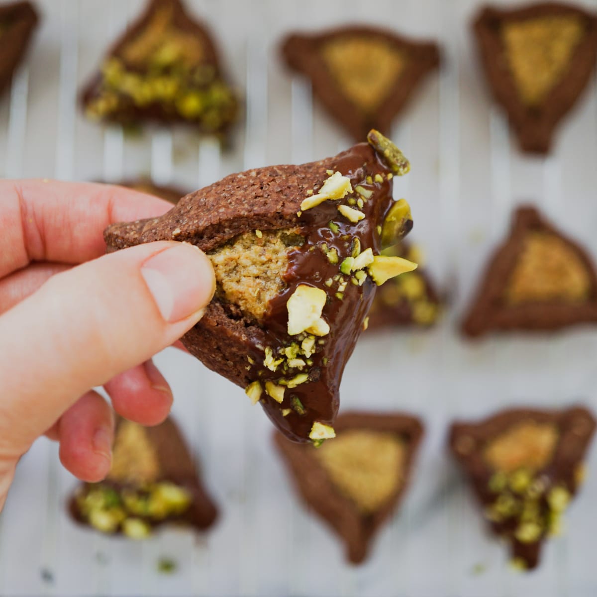 holding a chocolate hamantaschen with pistachio filling and chocolate cover