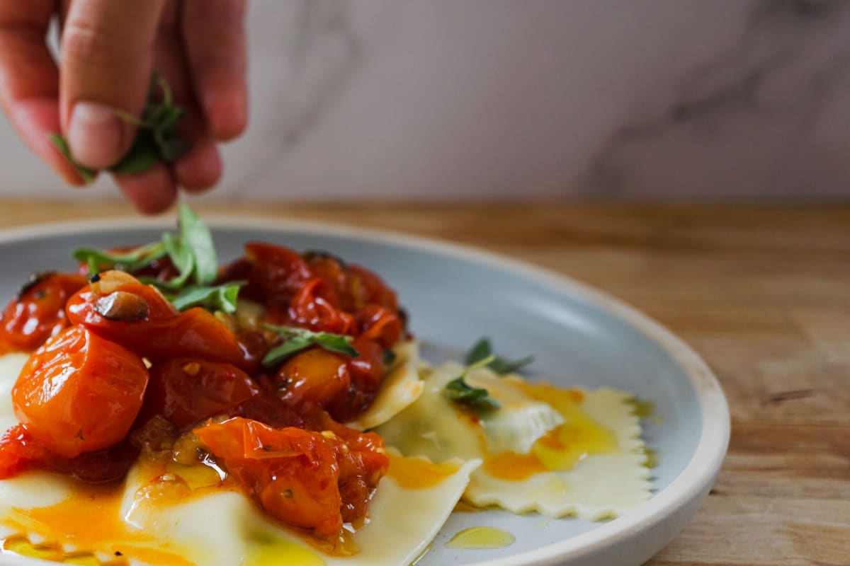 garnishing the ravioli and cherry tomato sauce with fresh oregano