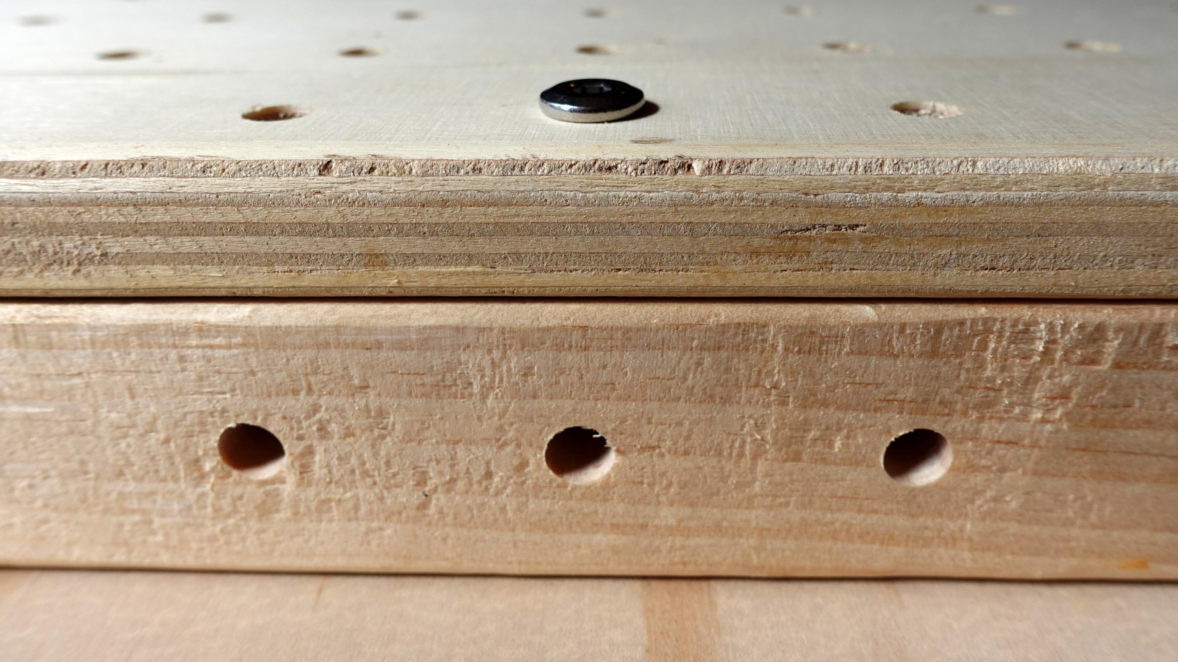 Two wooden beams are placed perpendicularly, joined with a metal bolt passing through a 18mm panel. The bolt's head is visible on top of the panel.