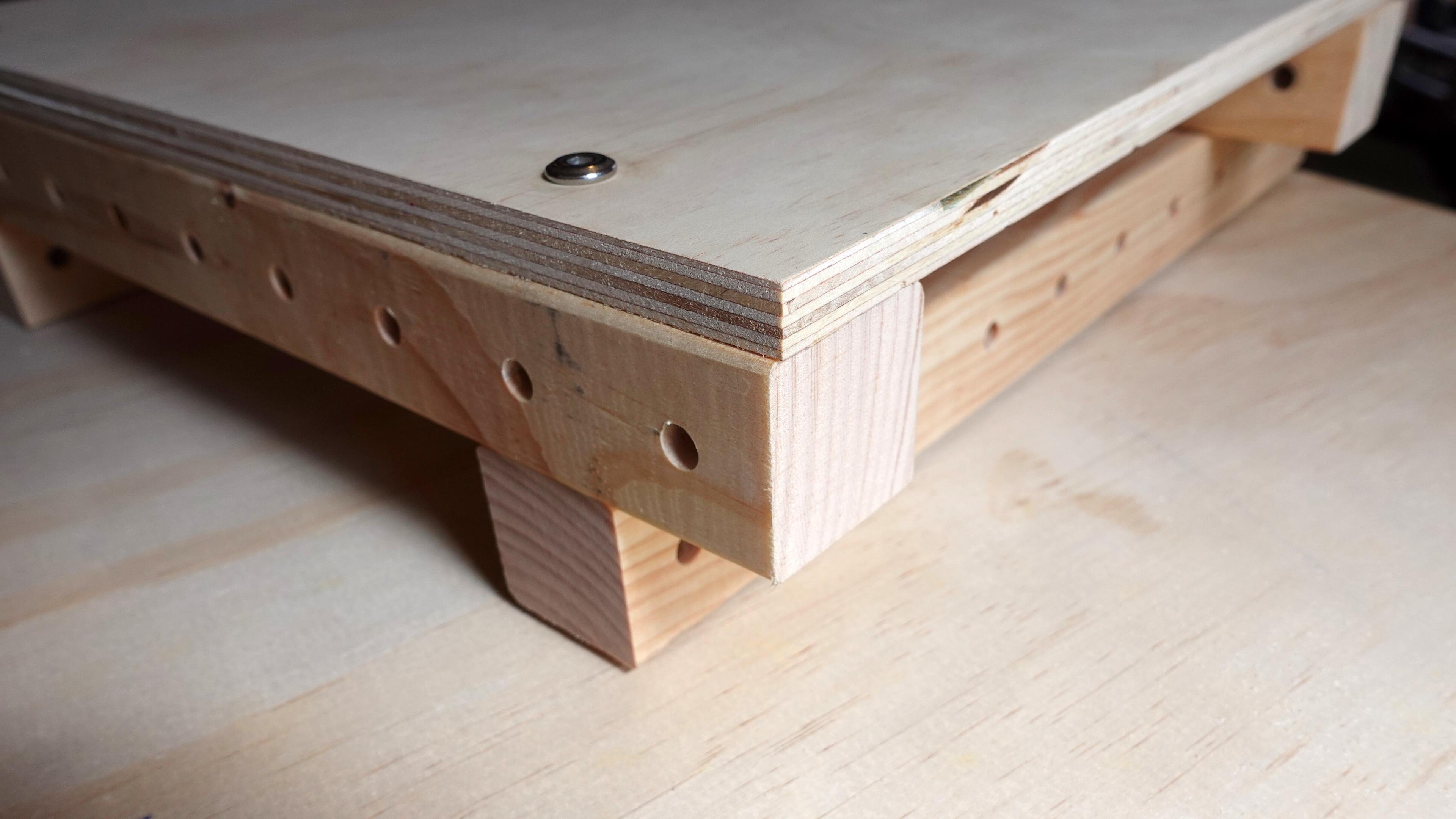 Two wooden beams are joined by a bolt passing through a 12mm panel, with a second beam visible beneath the panel, creating a stacked connection.