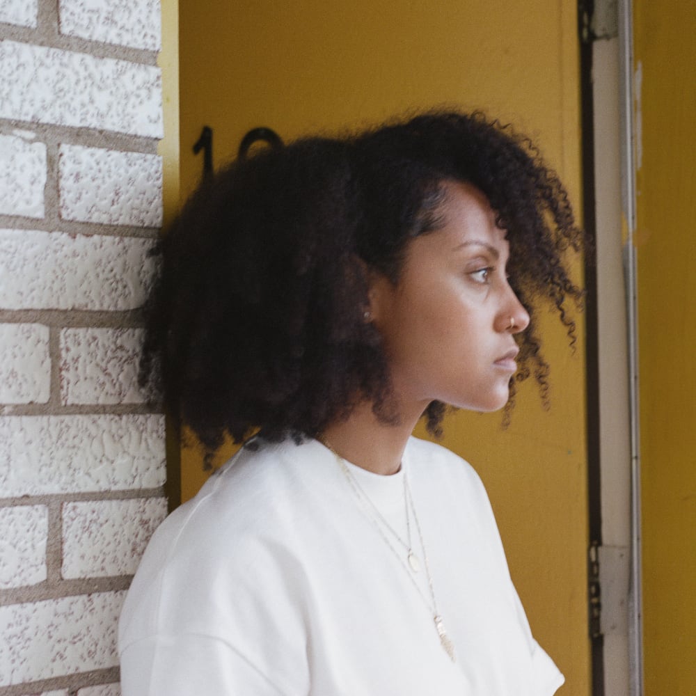 La chanteuse Naya Ali est devant un porte, le regard au loin.