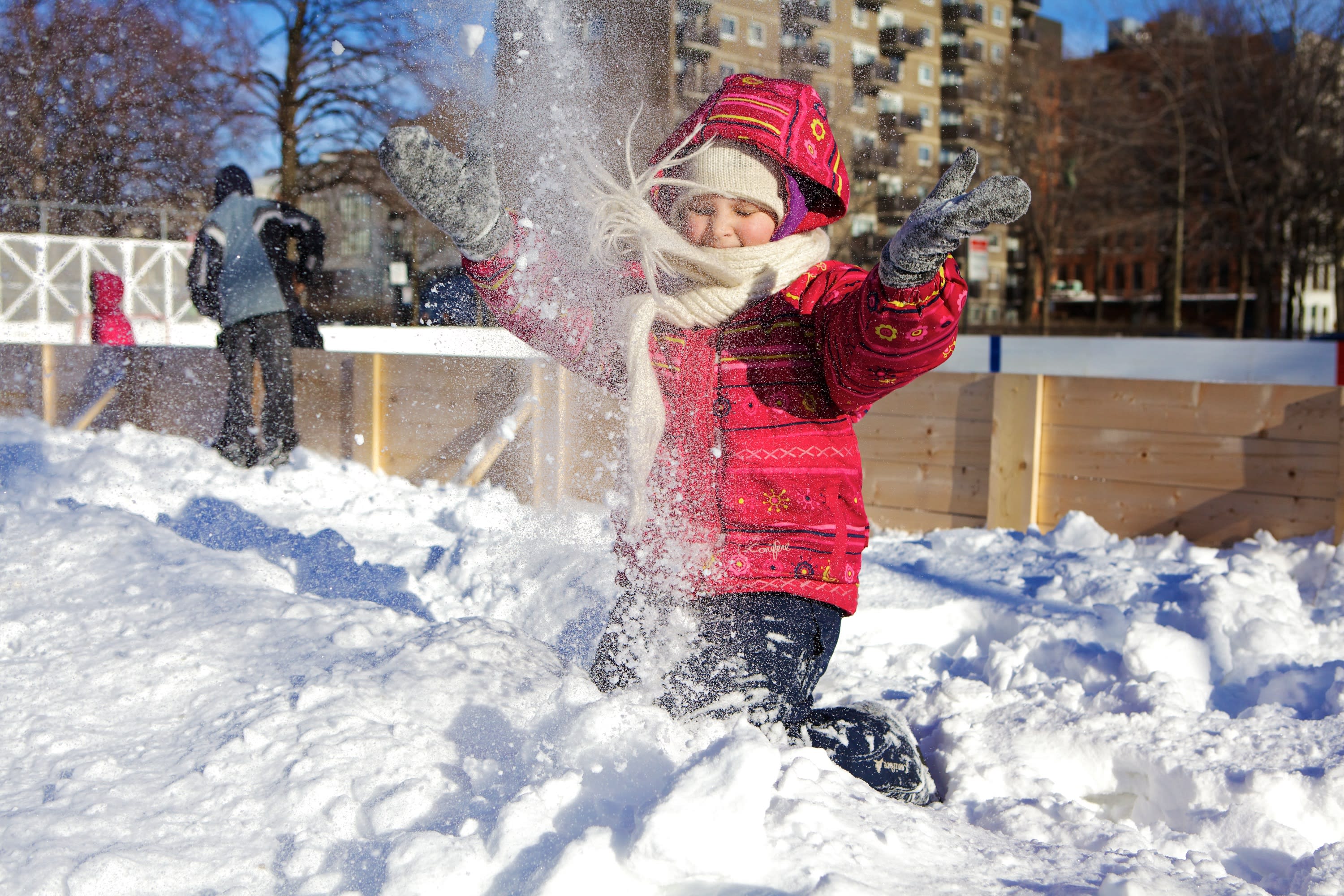 Une petite fille à genou dans un banc de neige lance de la neige dans les airs