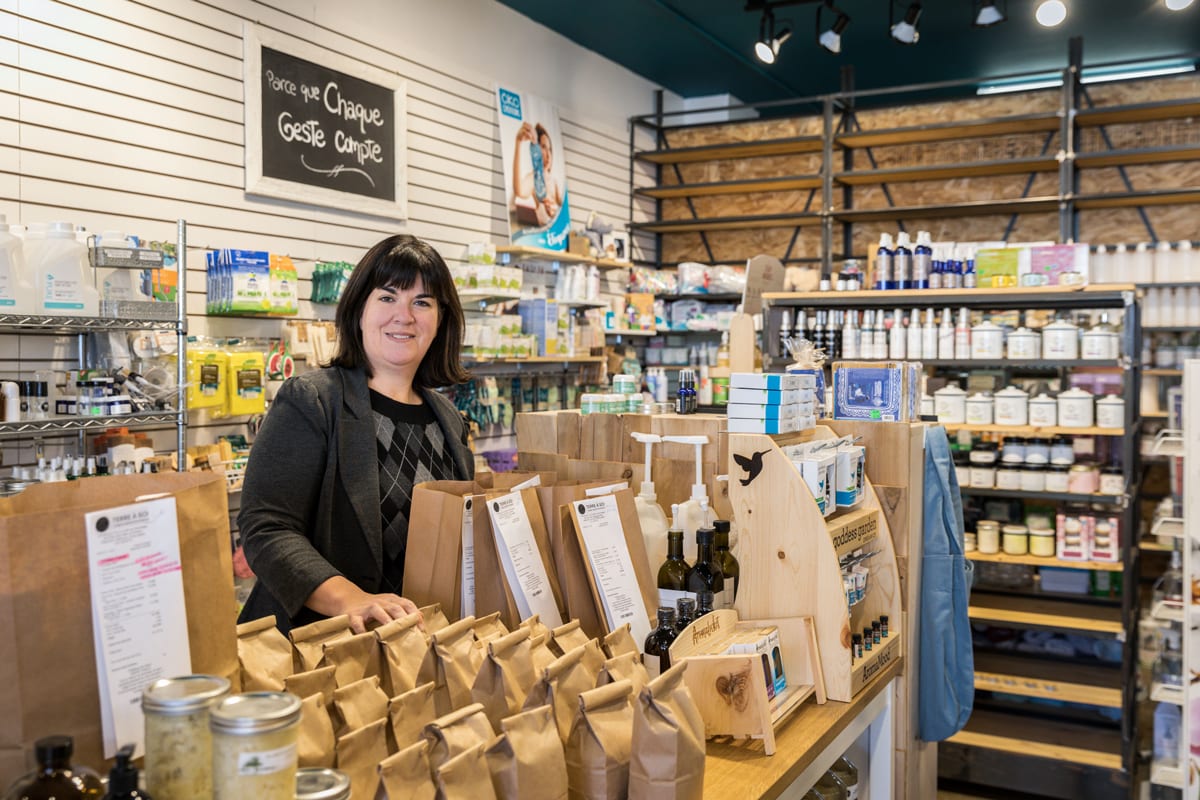 Une commerçante entourée de produits naturels et souriant à la caméra.