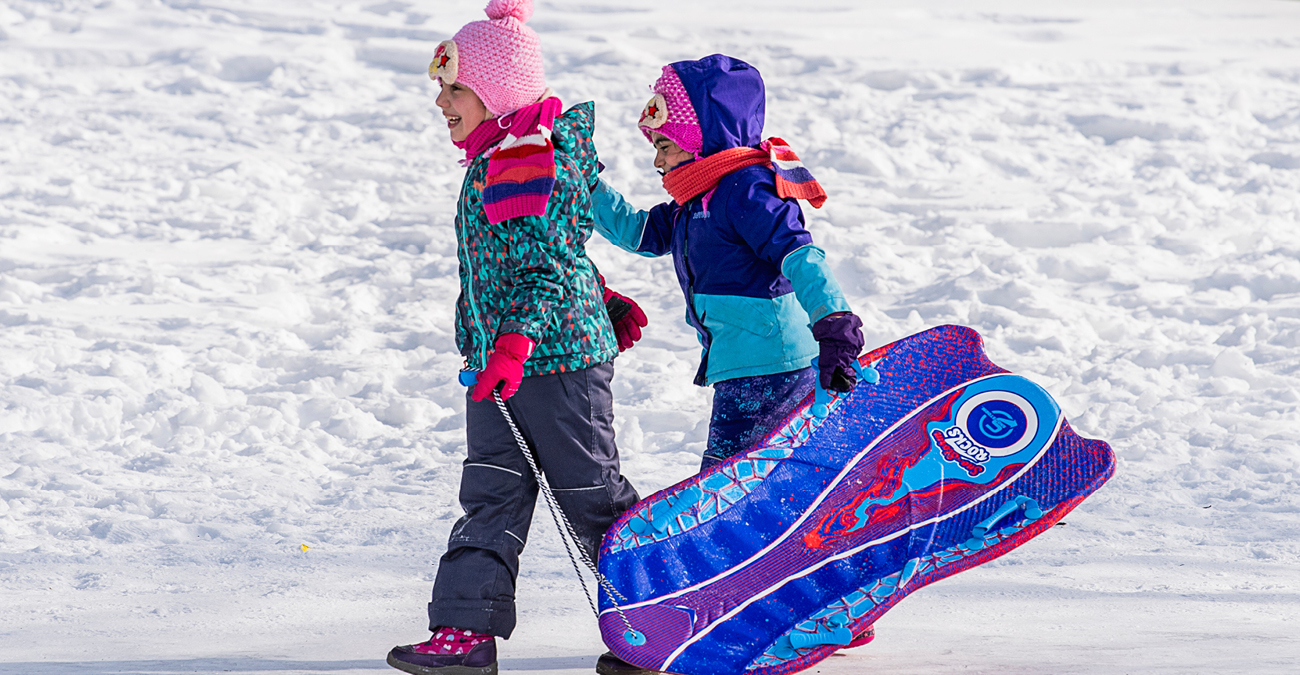 Two girls carry their sled on a sunny winter day.