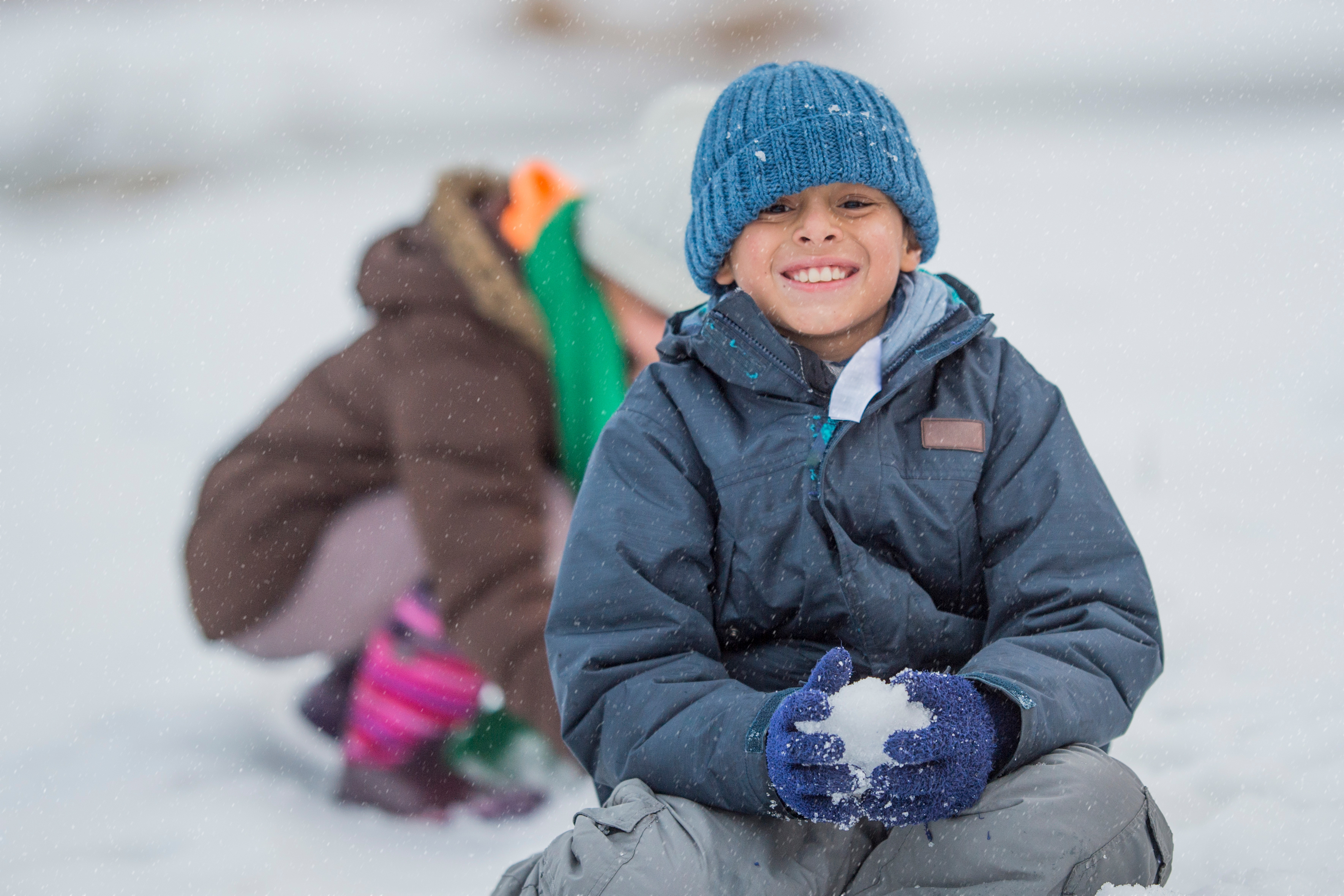 Jeune garçon en habit de neige joue, assis au sol dehors l'hiver.