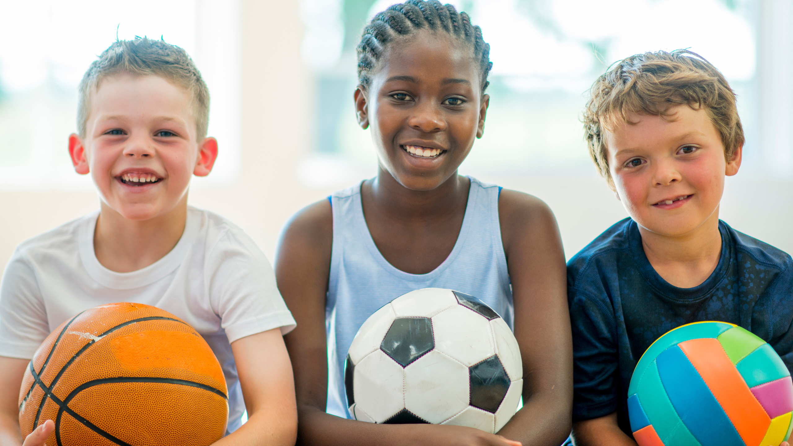 Trois enfants avec un ballon chacun basketball, soccer et volleyball