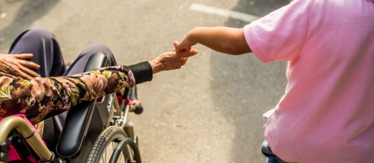 Une femme en fauteuil roulant tenant la main d'un enfant.