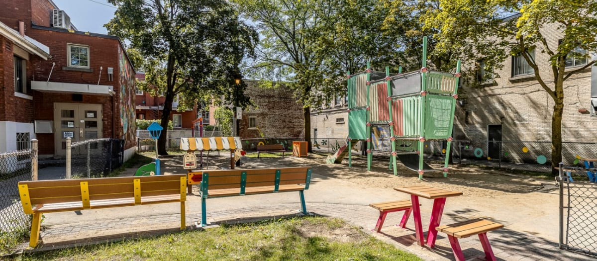 Photo d'un parc verdoyant montrant une grande structure de modules de jeux aux couleurs pastel ainsi que des bancs et une table à pique-nique de couleurs vives