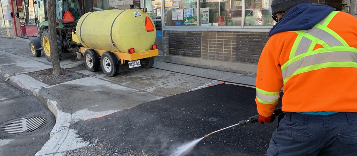 Un employé de l'arrondissement de Villeray–Saint-Michel–Parc-Extension nettoyant un trottoir