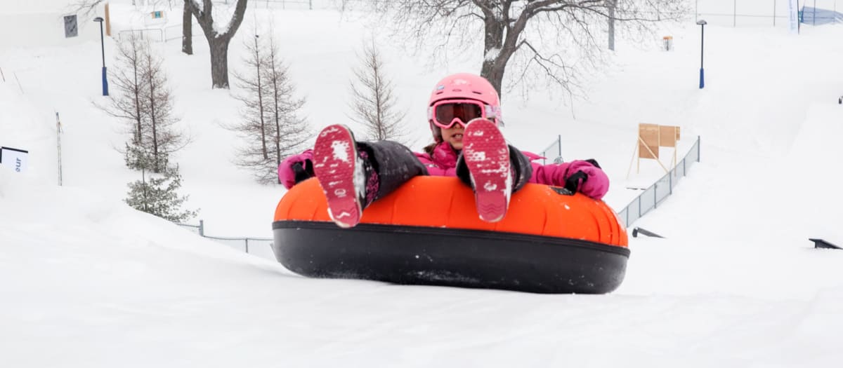 Un enfant en habit de neige dans un tube glissant d'une bute à neige