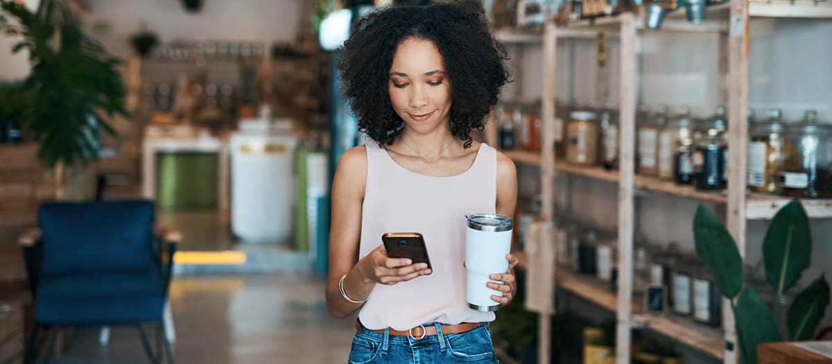 une femme sortant d'un café avec une tasse réutilisable