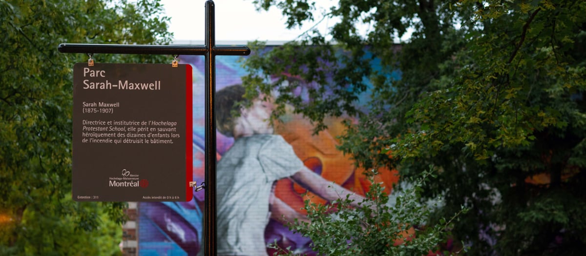 Panneau installé dans le parc Sarah-Maxwell, avec une murale en arrière plan.