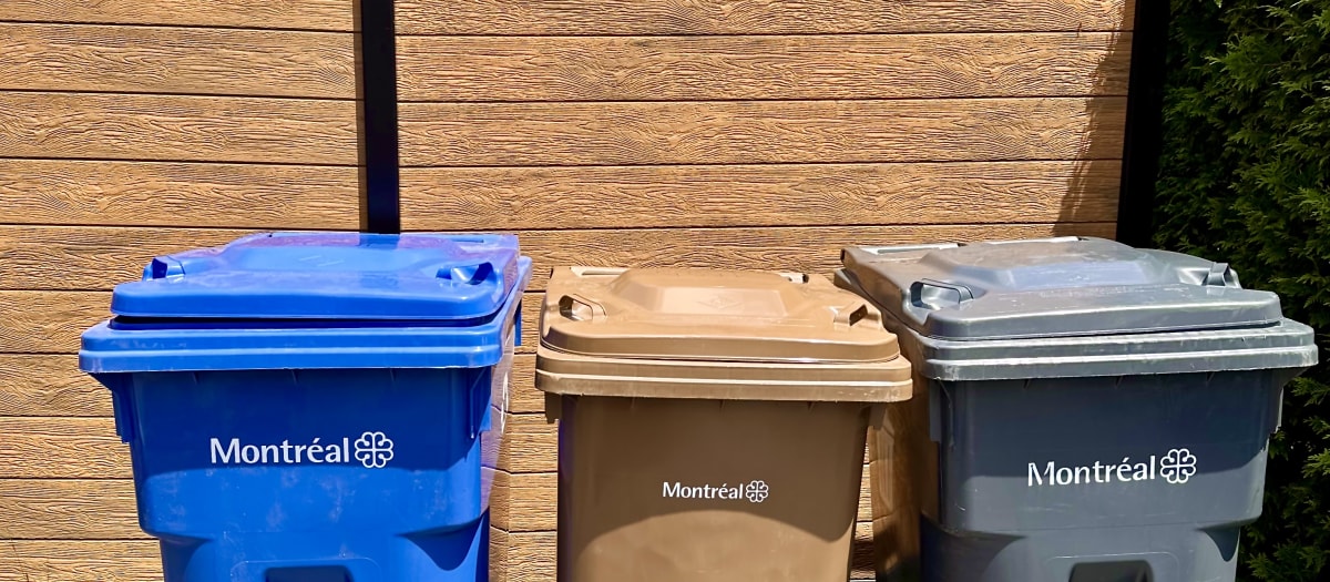 Trois bacs de collecte de couleur différentes : bleu, brun et gris, à l'effigie de la Ville de Montréal