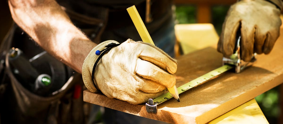 Un homme travaille et prend des mesures sur une planche de bois à l'extérieur de sa maison.