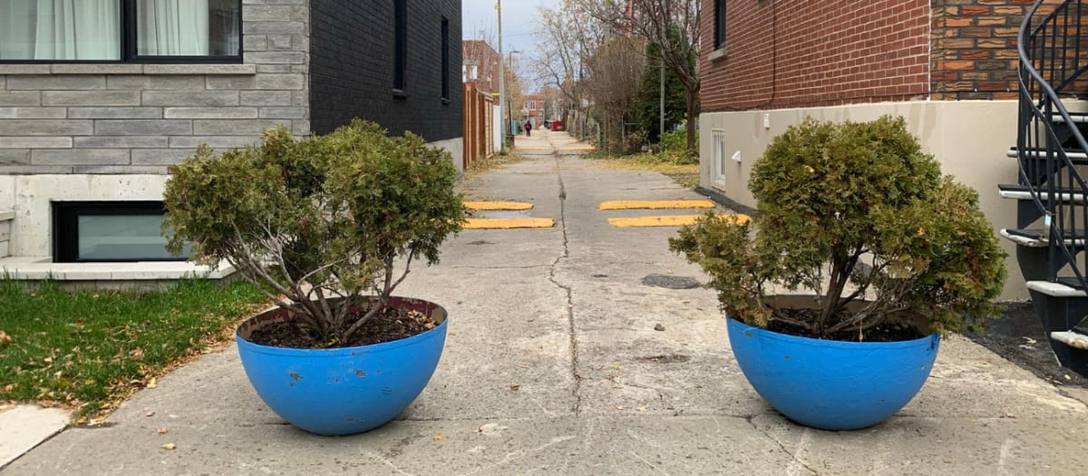 Deux bacs en béton hébergeant des arbustes bloquent l'accès d'une ruelle aux véhicules dans VSP