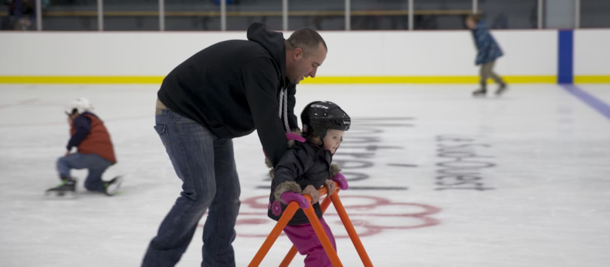 Un homme qui aide sa petite fille à patiner sur la glace