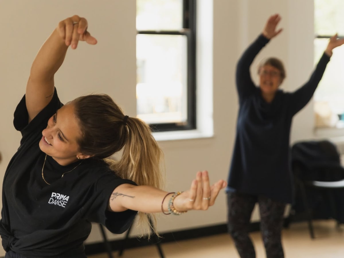 une jeune femme et une personne âgée qui exécutent le même mouvement de danse avec les bras en l'air