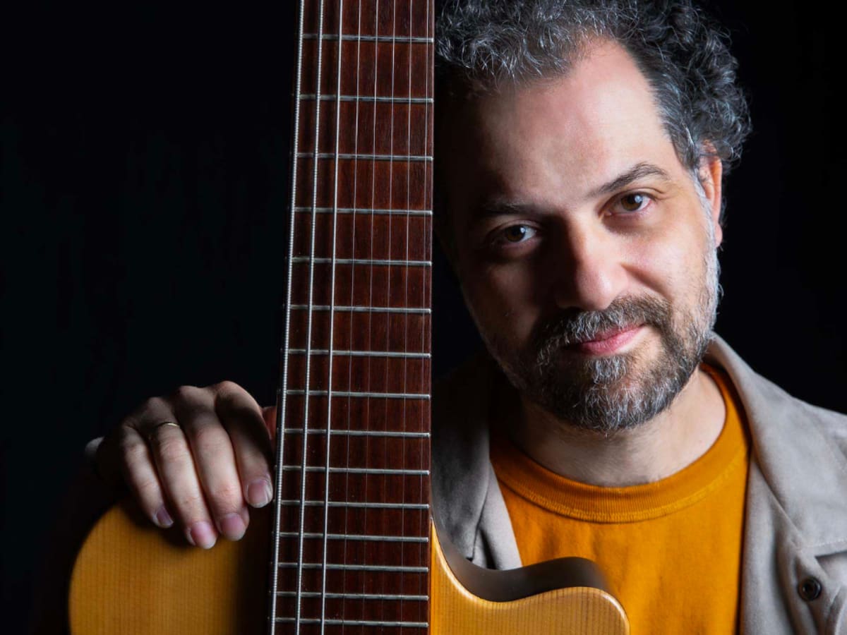 Homme tenant sa guitare près de lui sur fond noir.