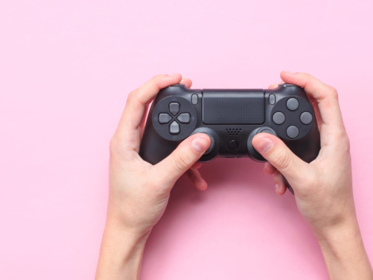 Des mains qui tiennent une manette de jeu vidéo, sur un fond rose.