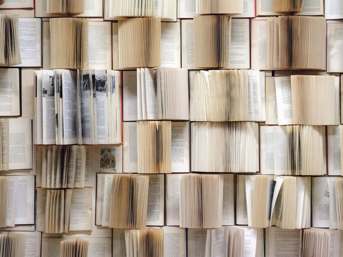 Plusieurs rangées de livres ouverts et superposés qui forment un assemblage dense de pages tournées.