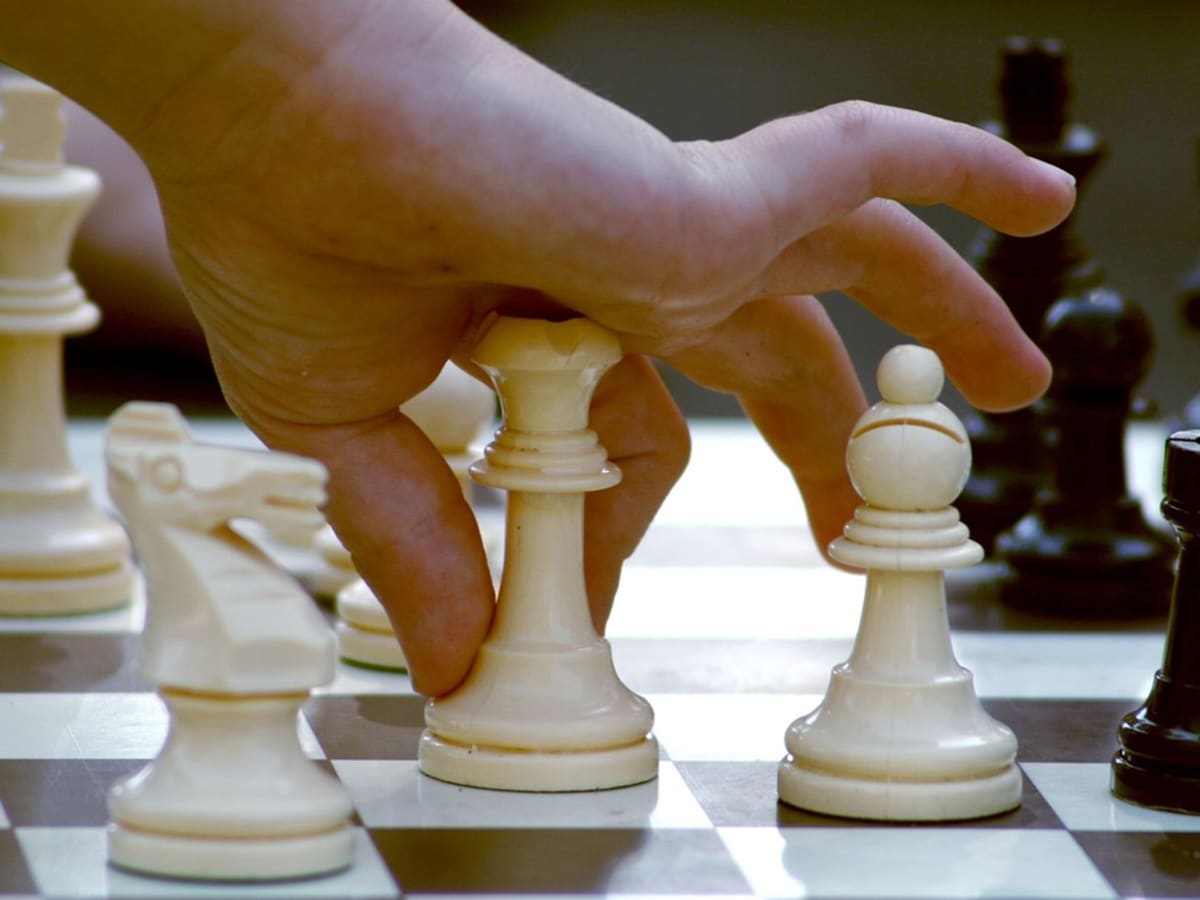 Une main déplace un pièce sur un jeux d'échecs.