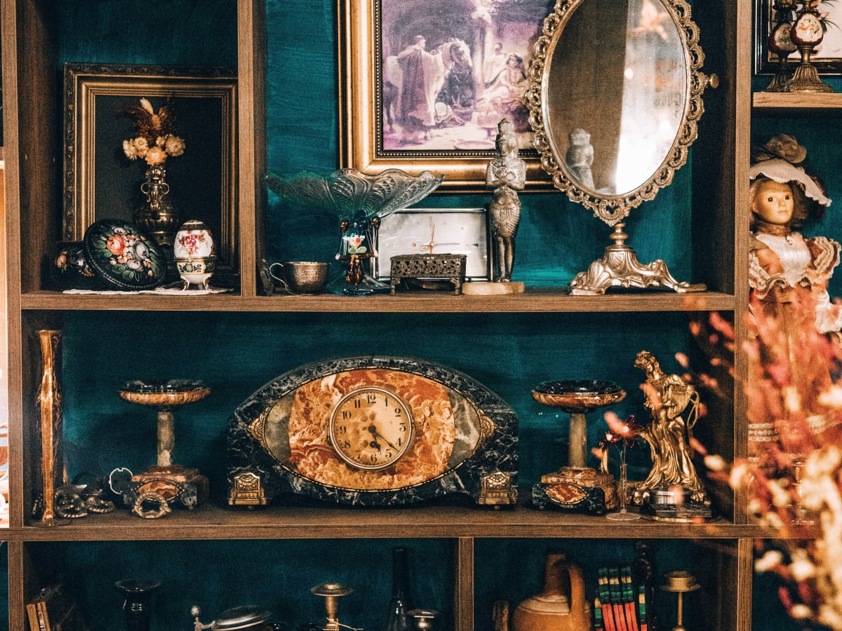 Cette image montre une grande étagère en bois à compartiments, remplie d'objets décoratifs anciens et de pièces de collection, donnant une ambiance de brocante ou de cabinet de curiosités.