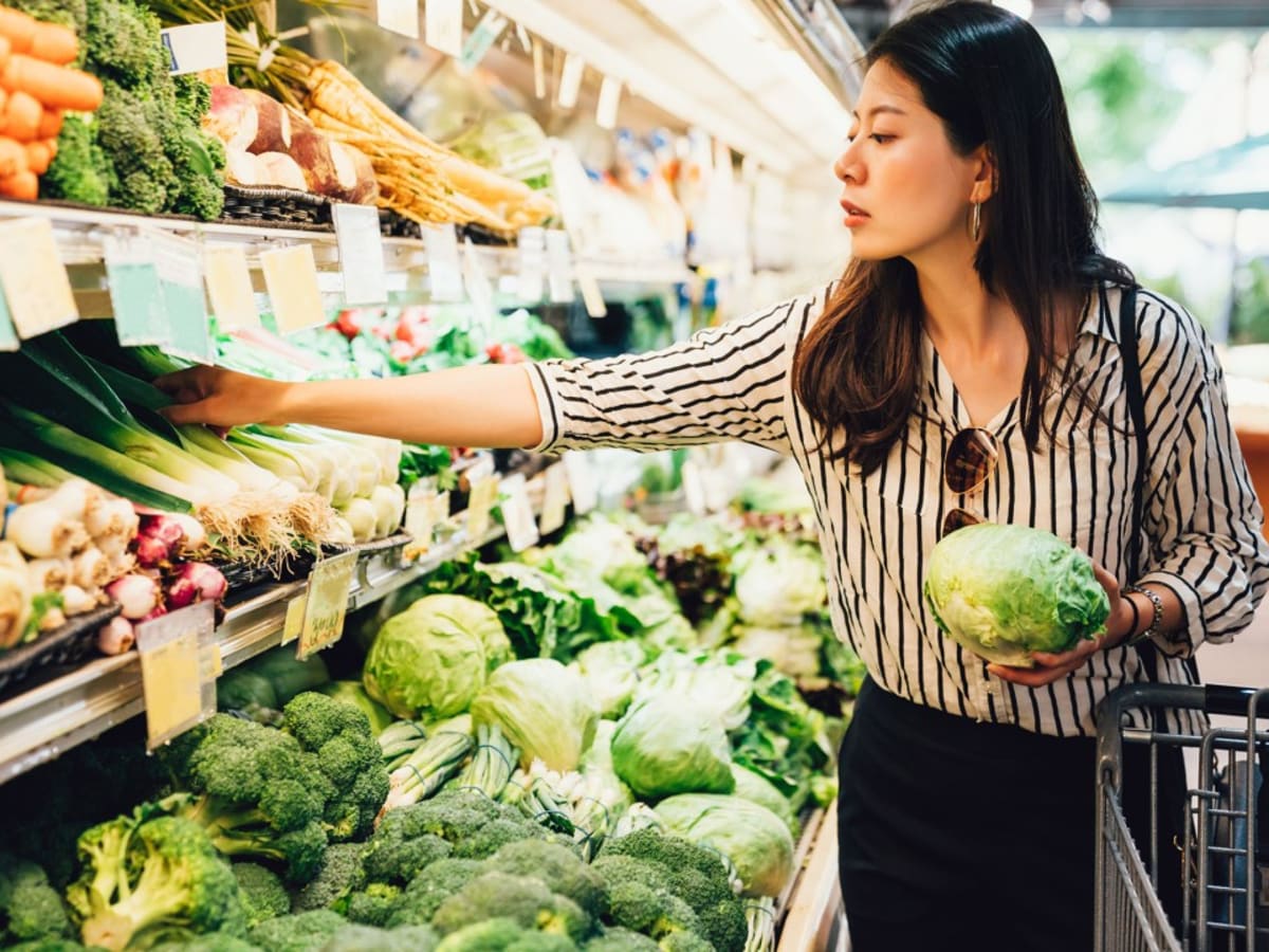 Une personne sélectionne des choux dans l'allée des légumes d'une épicerie